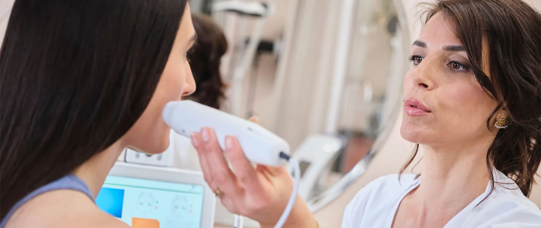 Une esthéticienne examine la joue d’une cliente avec un appareil de diagnostic